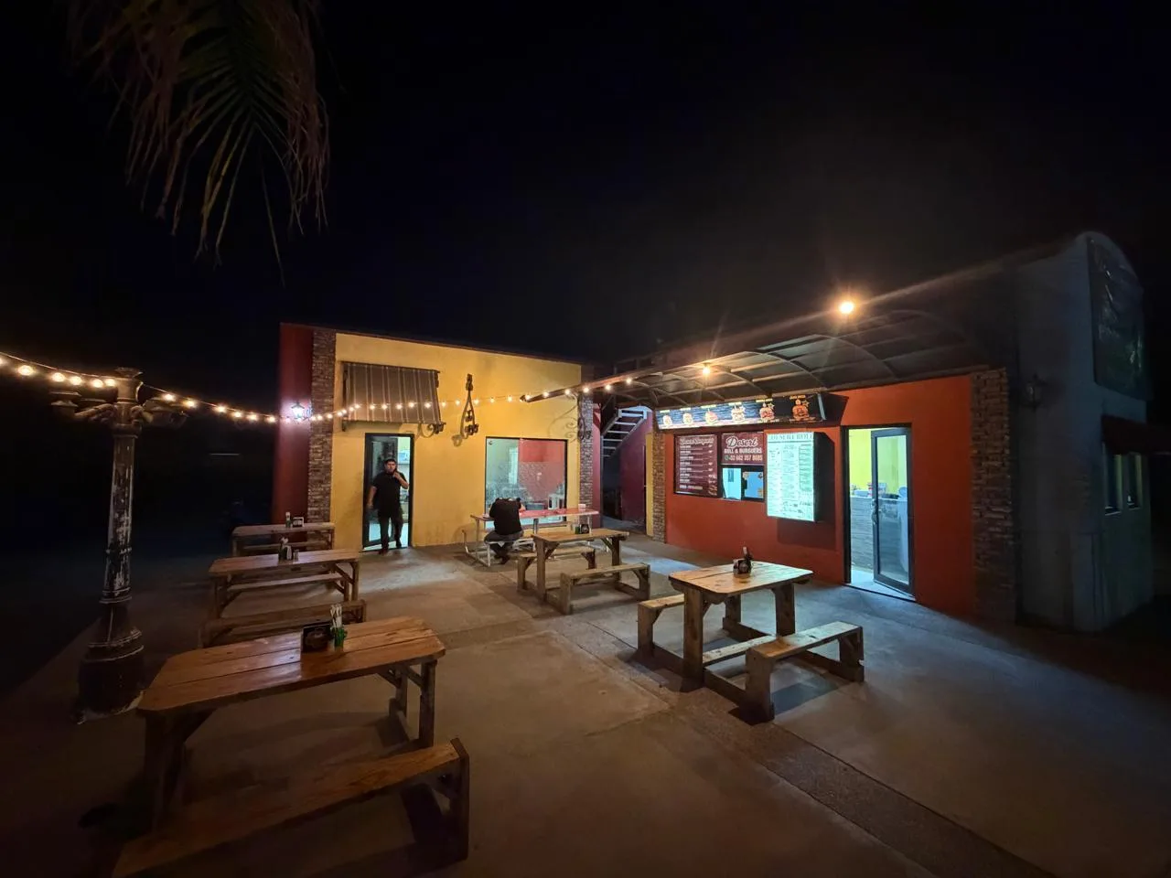 Patio nocturno de Desert Roll & Burguers con mesas de pino y luces en Las Minitas